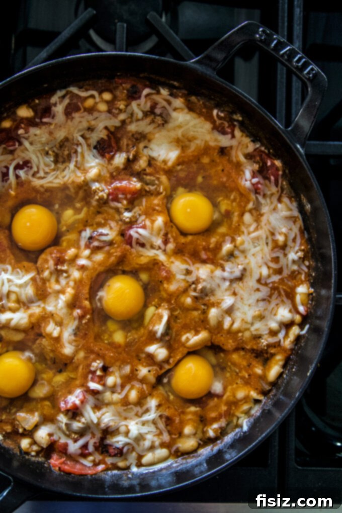 One-Pan Chorizo and White Bean Enchilada Bake 5 Eggs cracked into nests in the enchilada sauce, ready for baking.