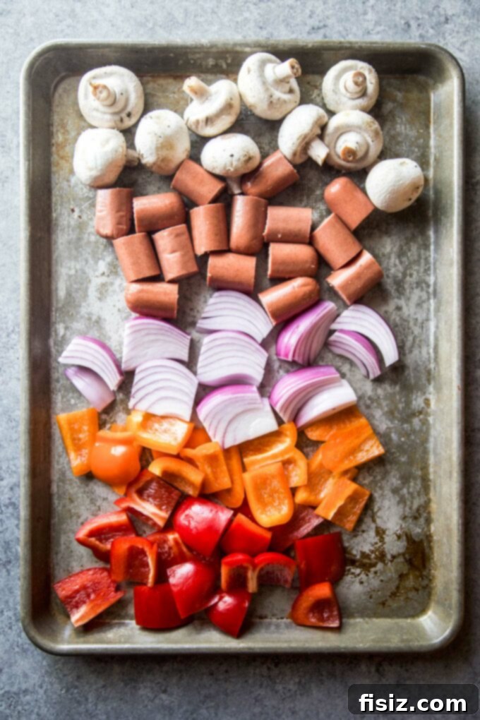 Epic Hot Dog Skewers 5 Freshly chopped bell peppers, red onion, and mushrooms alongside hot dog pieces on a sheet pan, ready for skewering.
