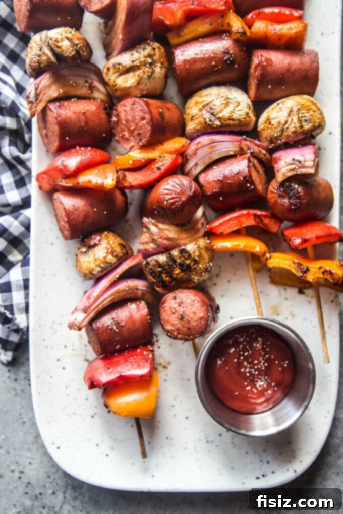 Epic Hot Dog Skewers 9 A vibrant close-up of a single Loaded Hot Dog Skewer, perfectly grilled and glistening with sauce, resting on a clean plate.