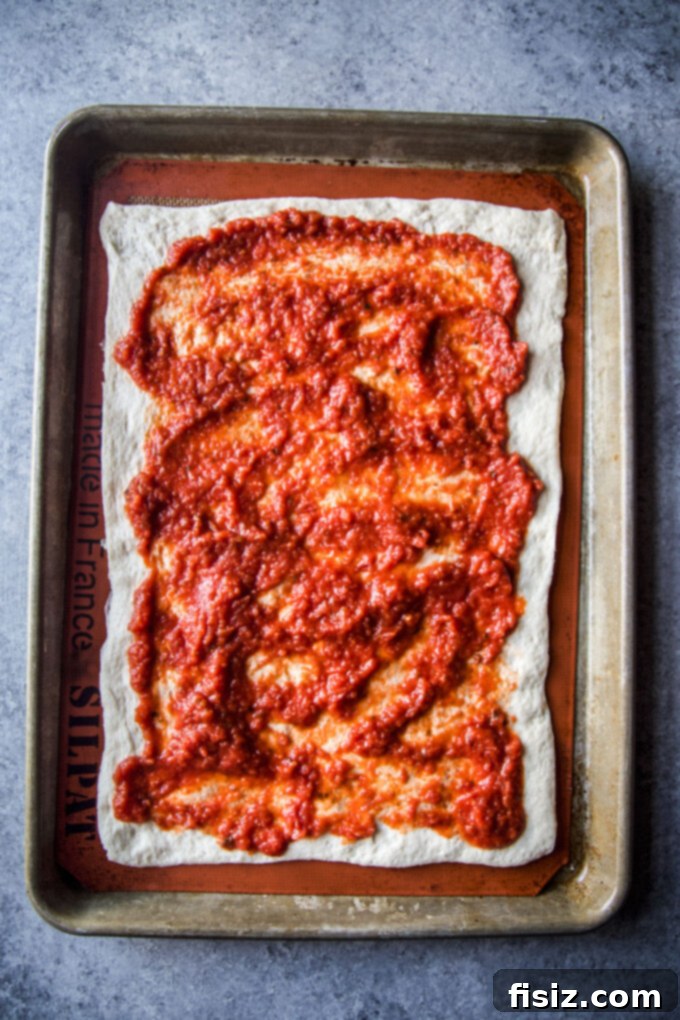 Pizza dough spread on a baking sheet with tomato pizza sauce evenly applied
