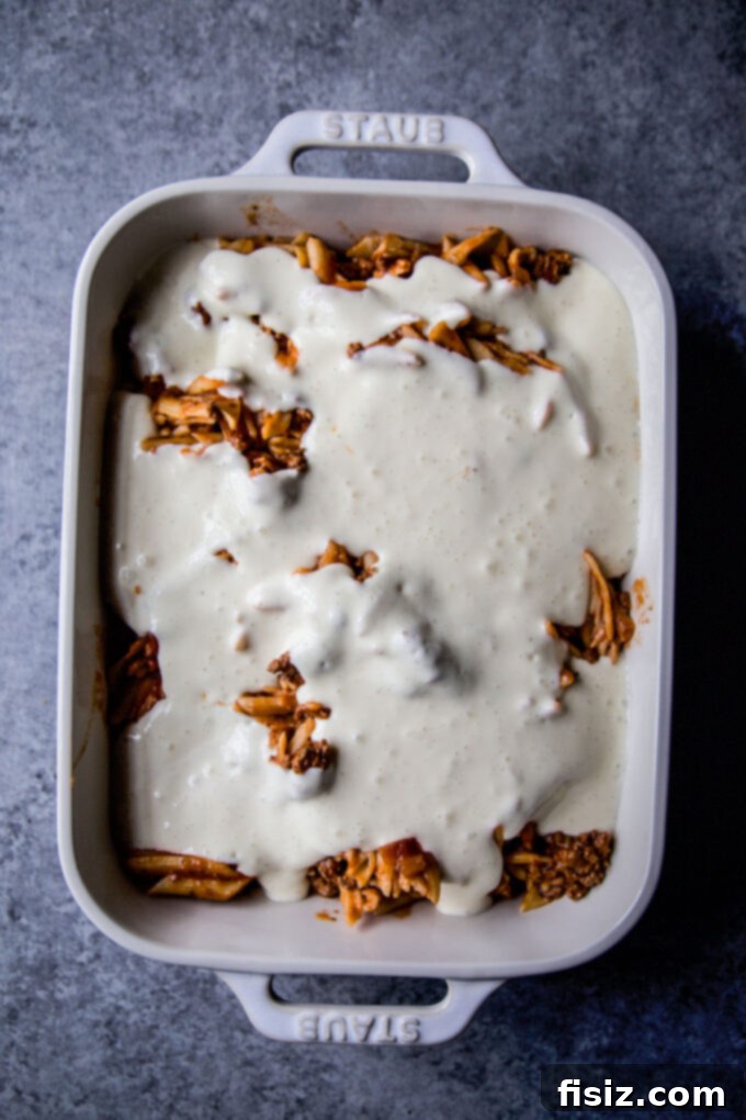 ziti lamb mixture covered in a creamy sauce before baking