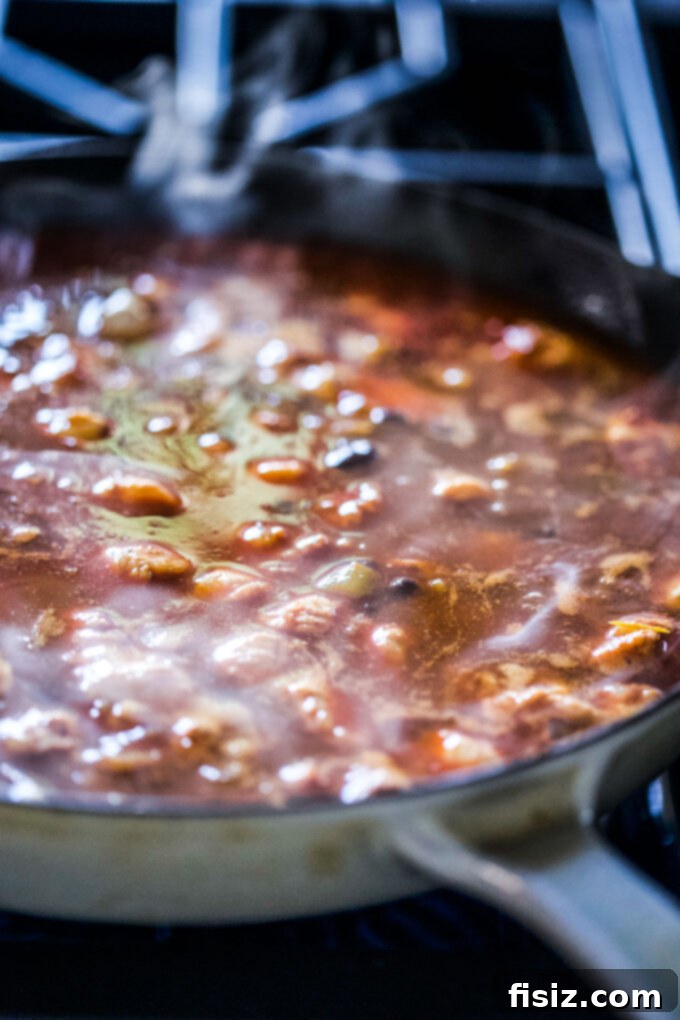 One Pan High Protein Chipotle Chicken Enchiladas 5 chipotle chicken cooking in a sauce