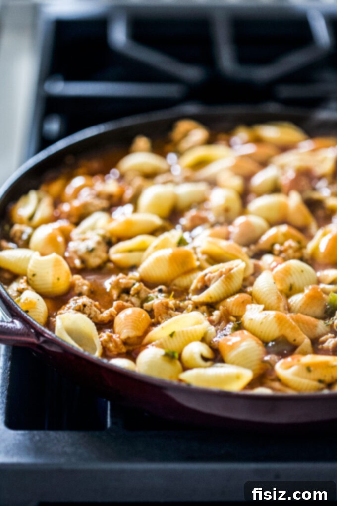 One-Pan Buffalo Chicken Chili Pasta 6 Pasta shells mixed into the buffalo chicken chili sauce in a skillet, topped with shredded cheese.
