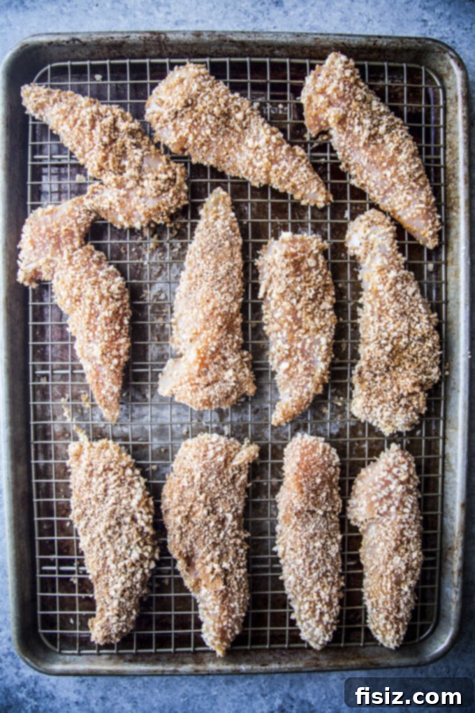 Zesty Indian Chicken Tenders with a Cooling Ranch Dip 5 Coated chicken tenders arranged on a baking sheet with a wire rack, ready for baking.