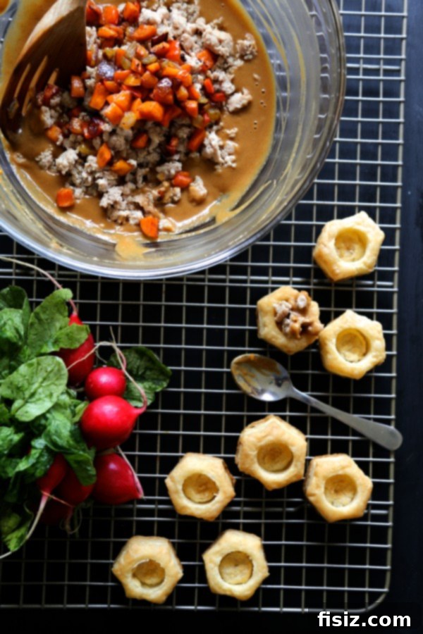 A serving of spicy Asian chicken puff pastry bites topped with vibrant roasted vegetables and fresh parsley.